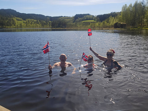 3 glade personer som står i vannet med hvert sitt flagg i hånda